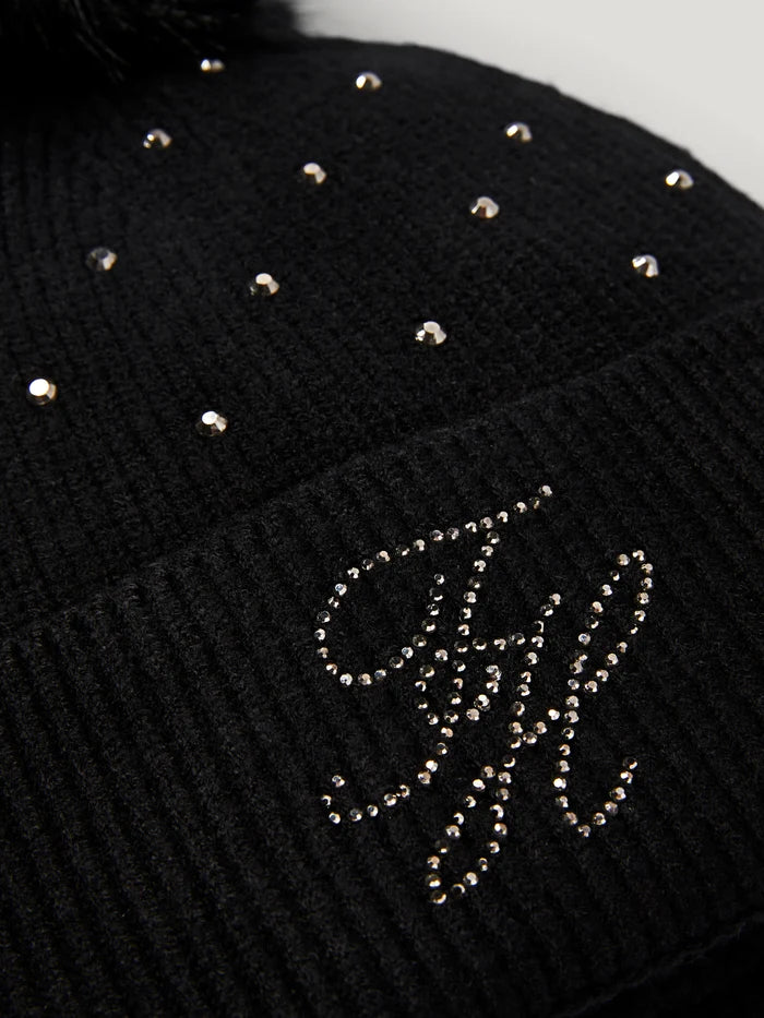 Close-up of a black Tommy Hilfiger Daly Women Rhinestone Pom Pom Beanie with rhinestone embellishments, including a large script monogram and scattered studs.